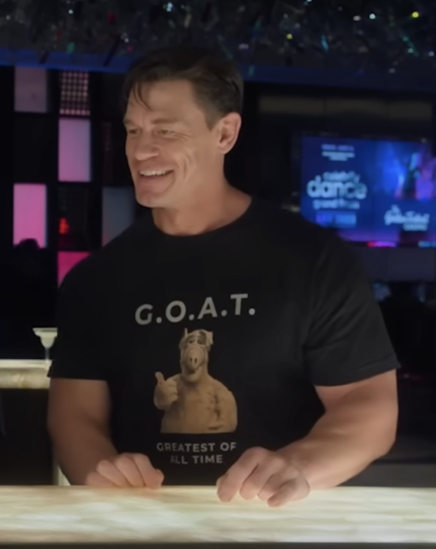 Ricky Stanicky or John Cena Wearing a shirt that says GOAT Greatest Of All Time with the Alf image