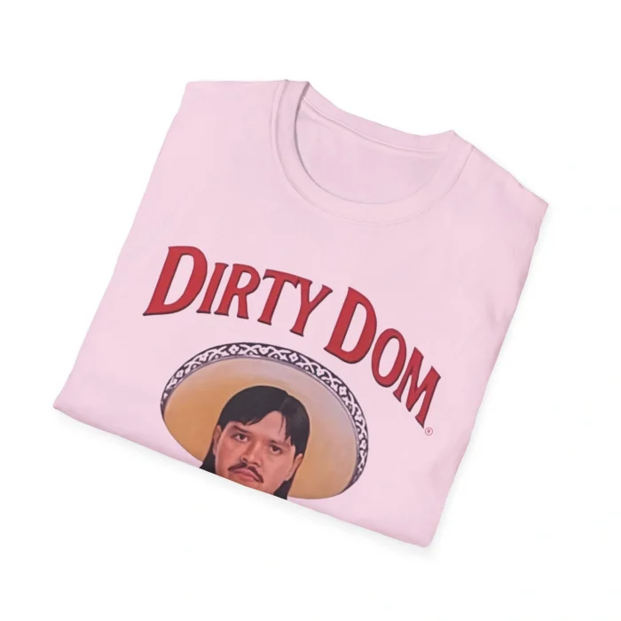 A folded light pink Dirty Dom Tapatío Shirt with bold red "Dirty Dom" text above a sombrero-wearing man's face illustration, shown on a white background.