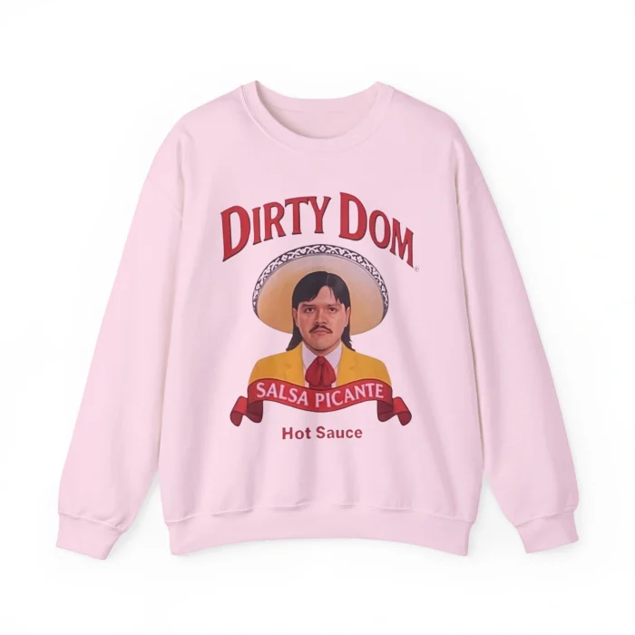 The Dirty Dom Tapatío Shirt features a man with a sombrero and mustache on light pink fabric. "DIRTY DOM" is printed above, and "SALSA PICANTE Hot Sauce" appears below in bold red, giving it a spicy, playful look.