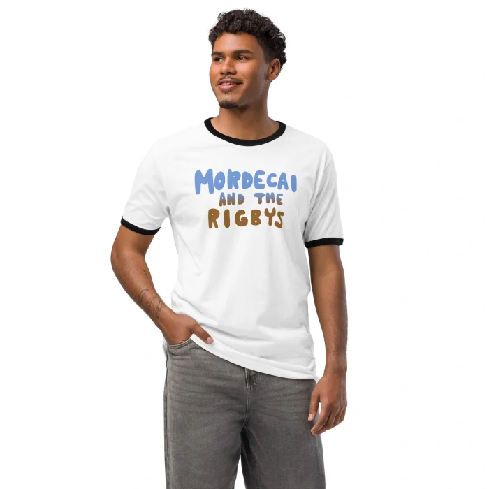 A man wears the Mordecai and the Rigbys Shirt, a white ringer tee with black collar and sleeves. The blue and brown text stands out as he smiles confidently with one hand in his pocket.