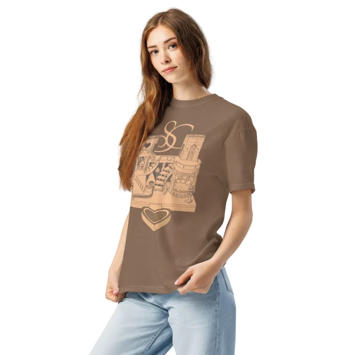 A young woman with long brown hair wears the Sabrina Carpenter House Tour Shirt—featuring tan graphics on brown—paired with light blue jeans, posing with one hand in her pocket against a plain white background.
