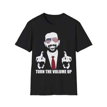The Zohran Mamdani Turn The Volume Up Shirt is a black tee with a graphic of a smiling man in suit and flag sunglasses, flashing both middle fingers. Below, bold text reads: TURN THE VOLUME UP—perfect for making a statement.
