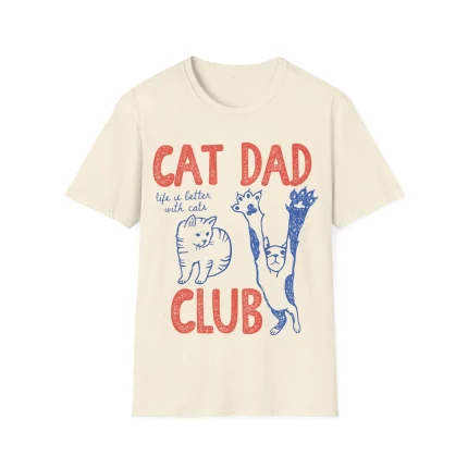 The Cat Dad Club Shirt is cream-colored with red "CAT DAD CLUB" text and blue "life is better with cats" lettering, plus two playful blue cat illustrations—one sitting, one stretching—perfect for cat lovers.